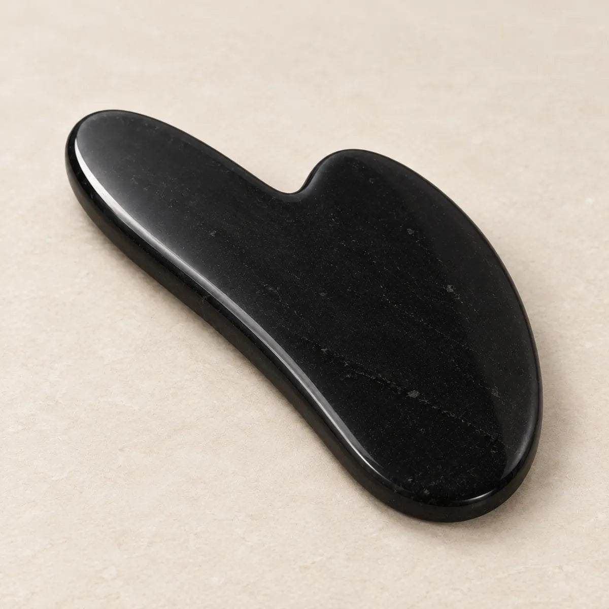 Strumento Gua Sha per il viso in shungite, su fondo chiaro