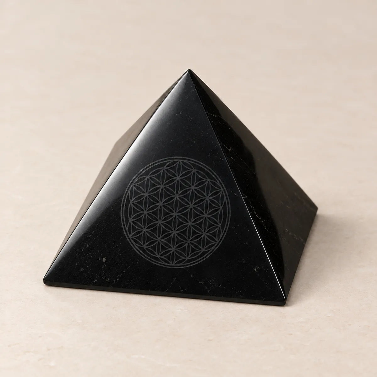 Piramide lucidata con Fiore della Vita inciso in shungite, su fondo chiaro