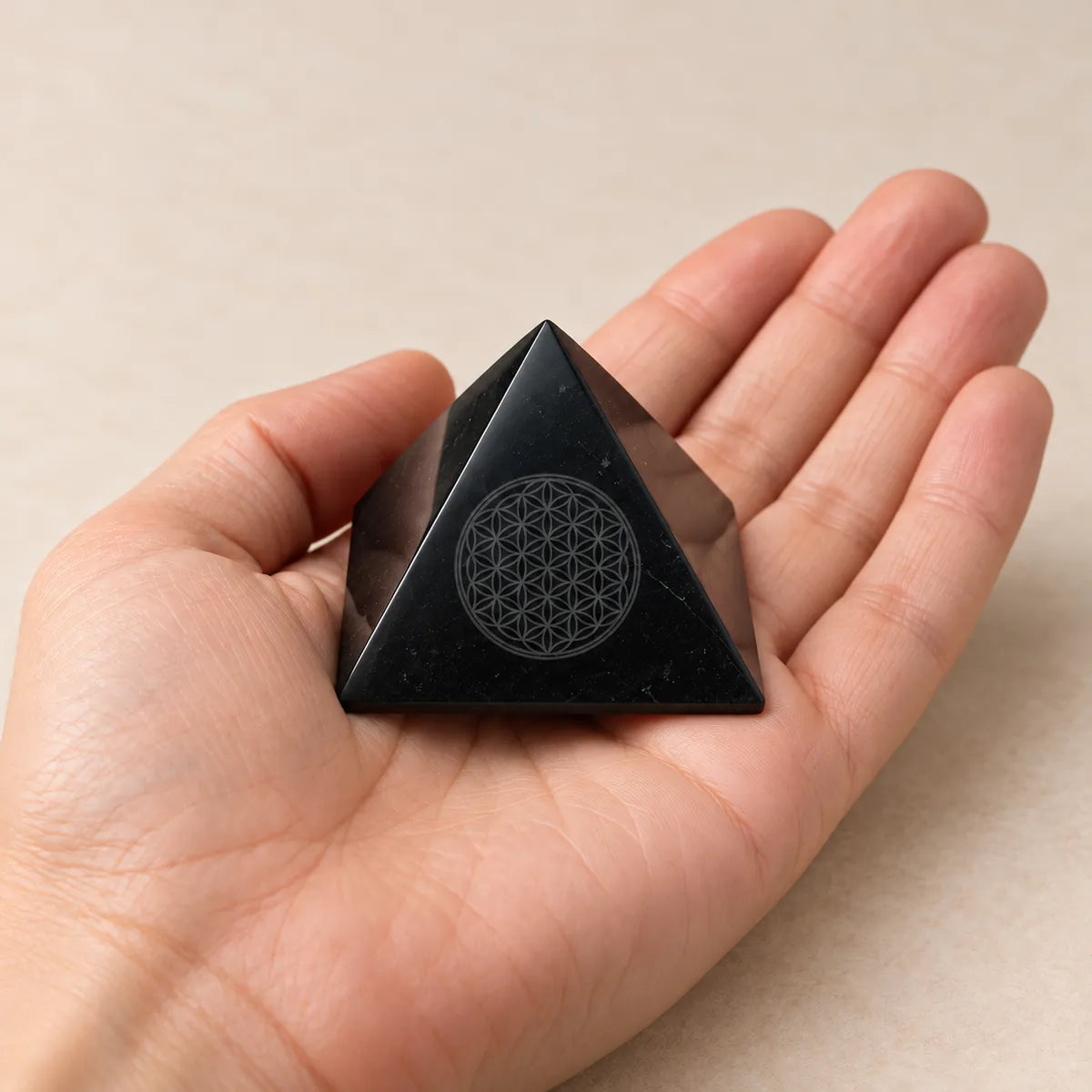 Piramide lucidata con Fiore della Vita inciso in shungite, tenuta in mano