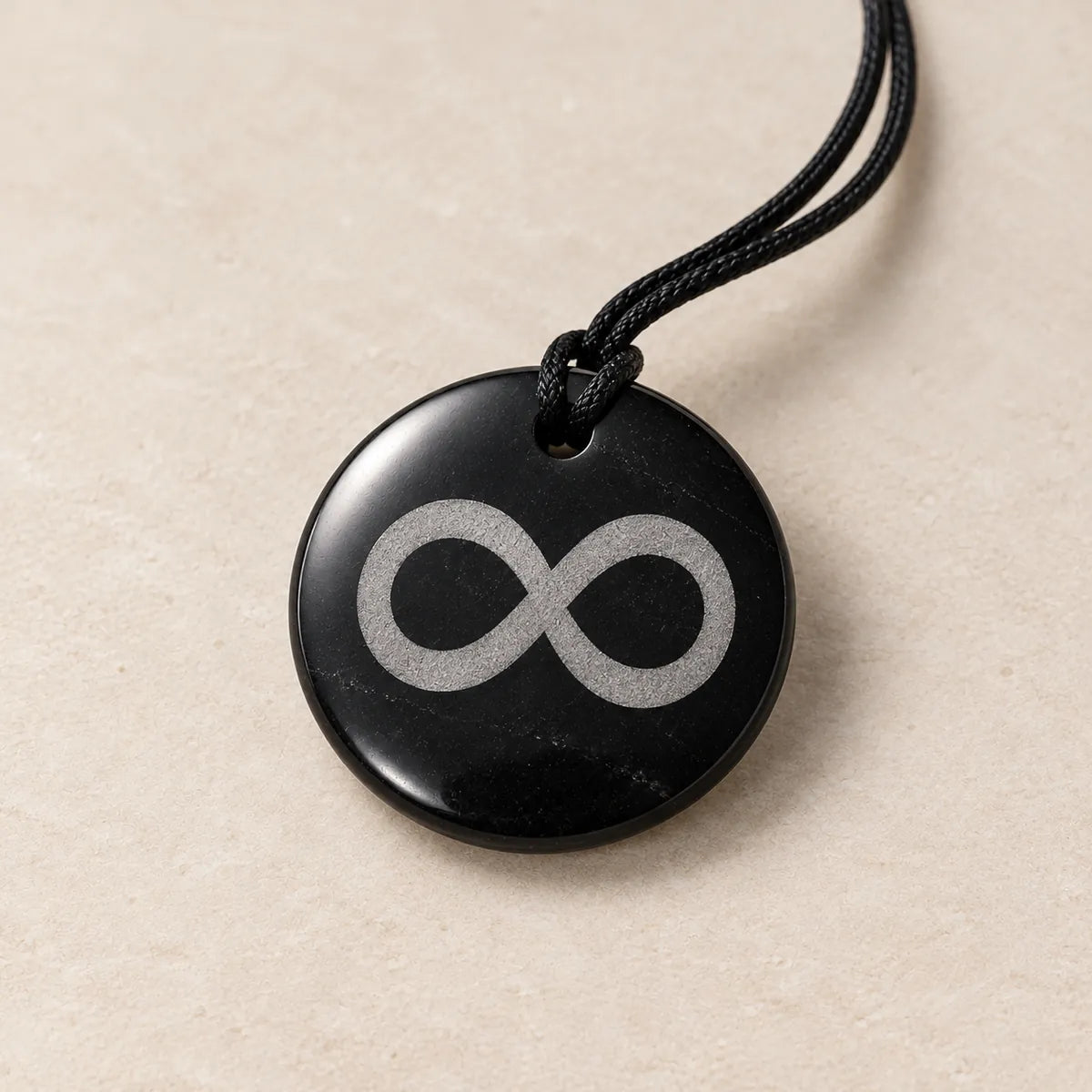 Pendente cerchio 30 mm inciso in shungite, Eternità, su fondo chiaro