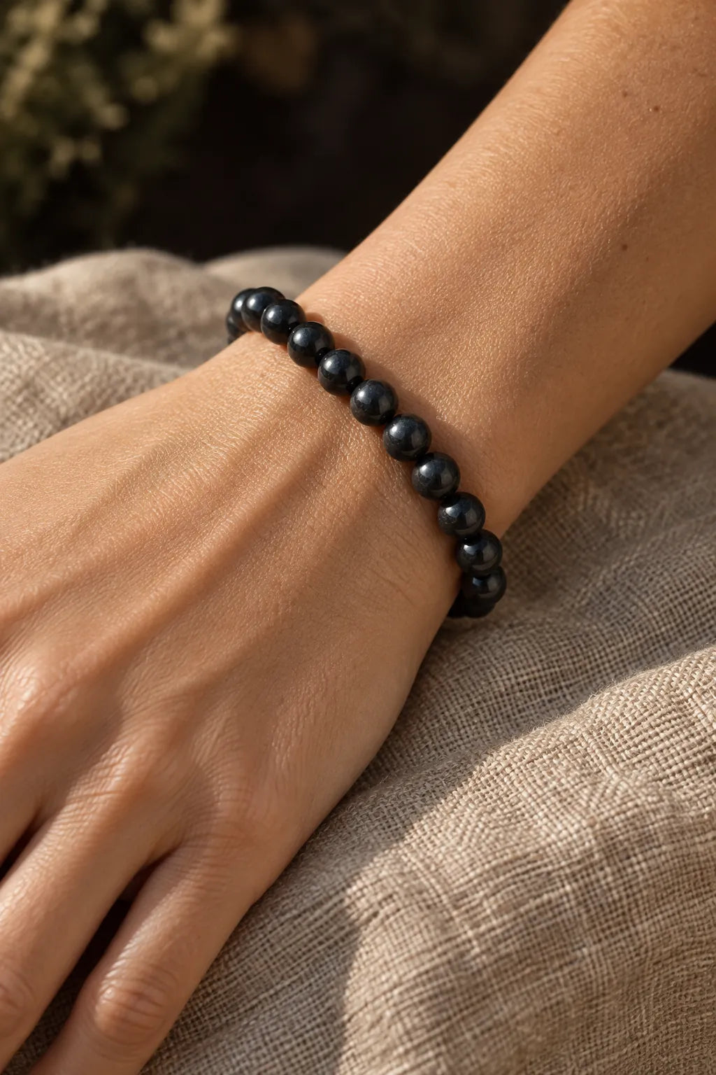 Bracciale di perle nere indossato al polso, accanto a una manica in lino