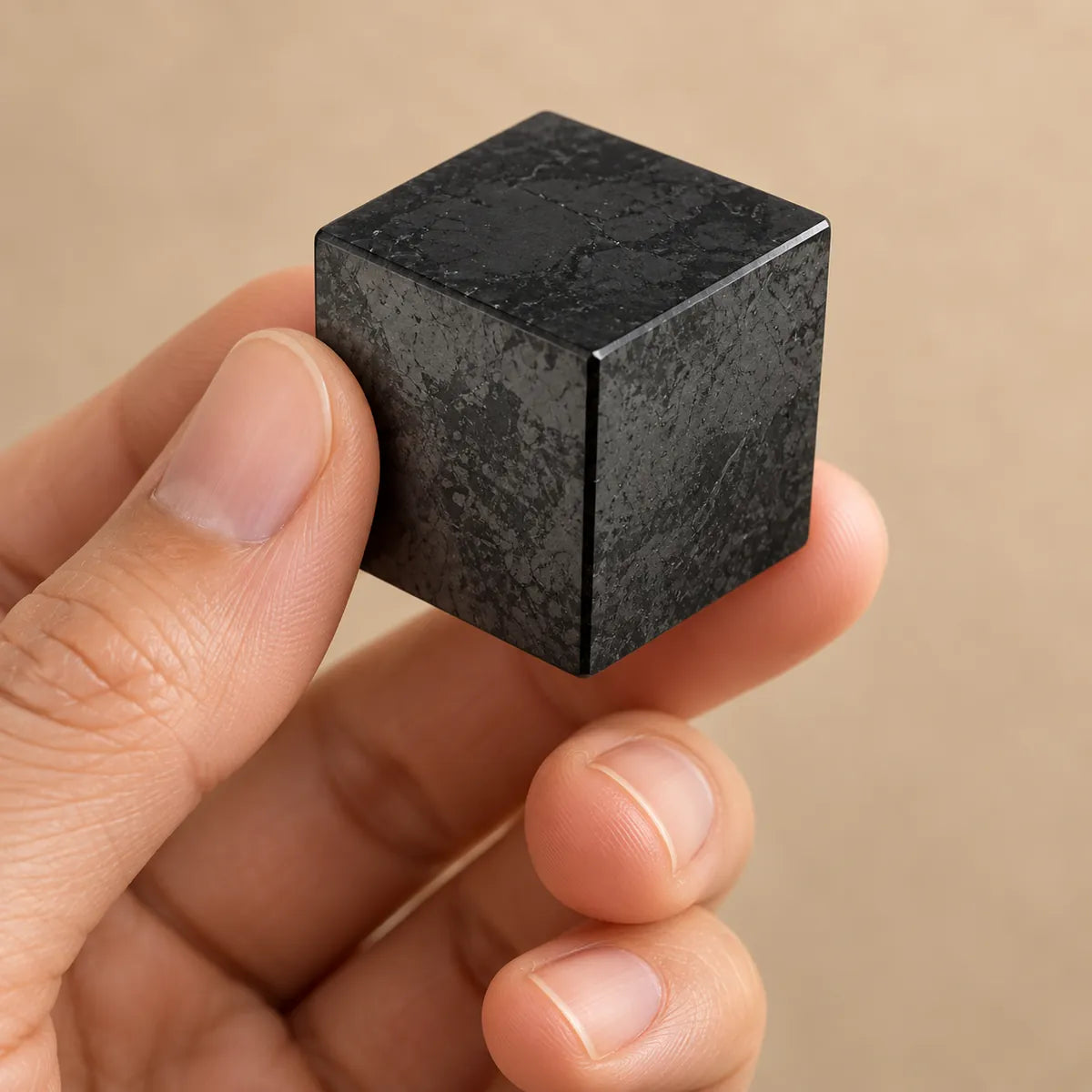 Piccolo cubo di shungite tenuto delicatamente tra le dita