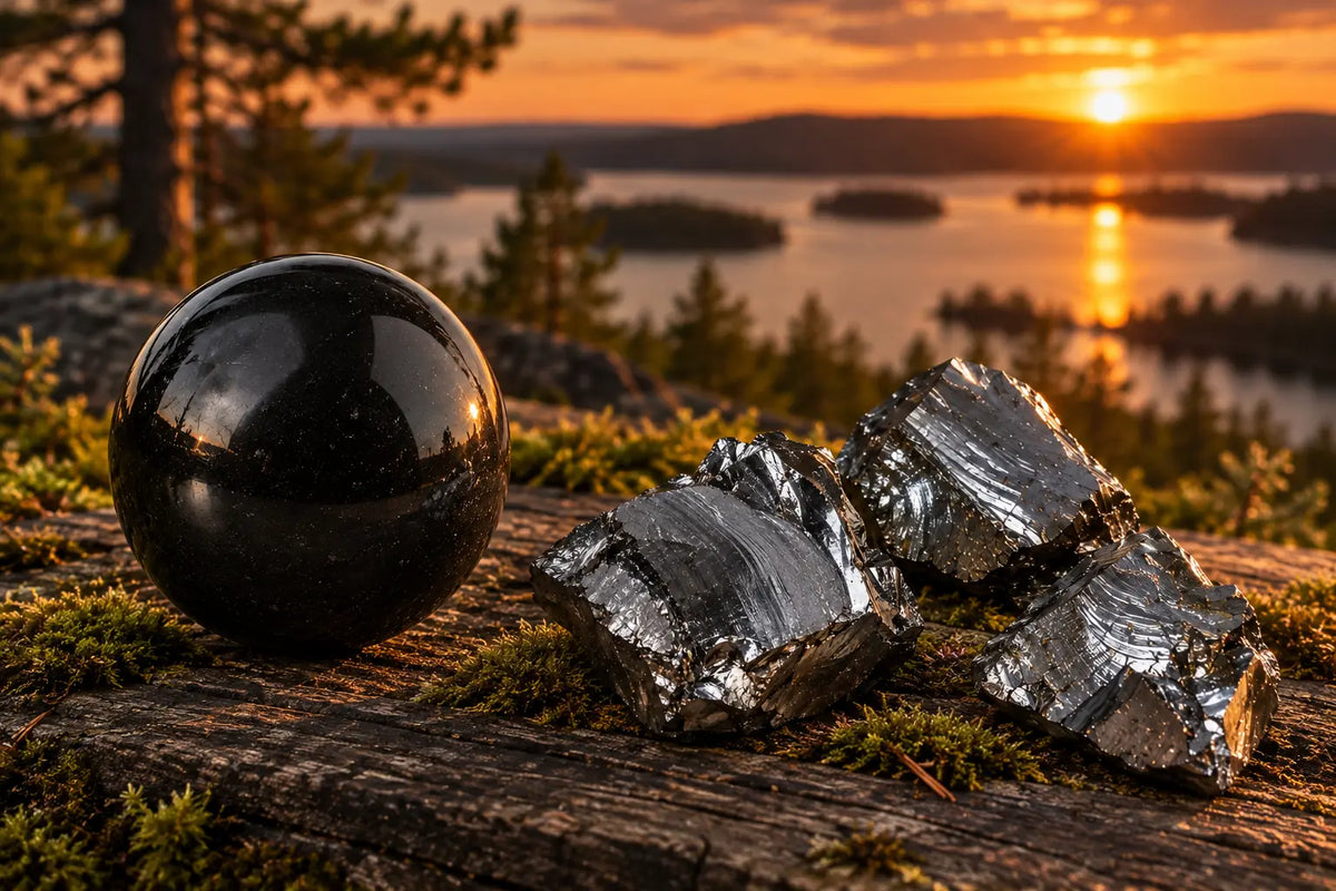 Una sfera di shungite lucidata e frammenti di Elite su una roccia, davanti a un lago al tramonto